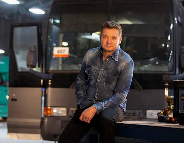 Jeremy Renner on set of Rennervations, a bus behind him and some power tools to one side (Credit: Disney+)
