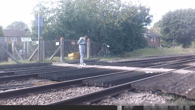 Teen stares at phone while stood on level crossing. Network Rail 