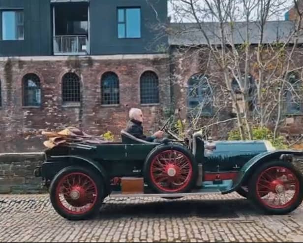An antique car driving down a cobbled street