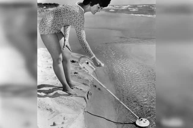 A woman using a metal detector to search for treasure at the beach in 1974