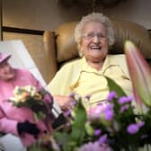 Edna celebrating her birthday surrounded by flowers and with a card from The Queen.