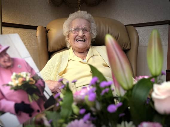 Edna celebrating her birthday surrounded by flowers and with a card from The Queen.