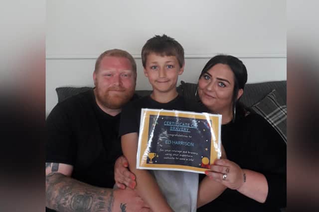 Eli Harrison with his dad Ian and mum Kayleigh and a certificate Kayleigh's colleagues made for Eli when they heard about his brave actions.
