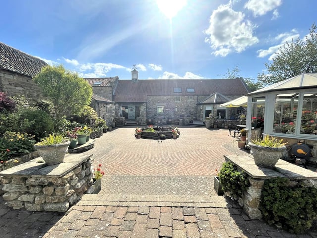 The setting of the paved garden with filled borders containing flowers, plants and shrubs.