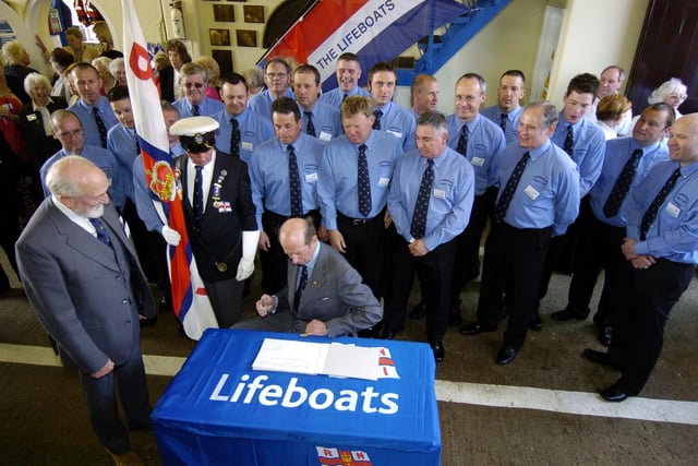 The Duke of Kent visits the RNLI Scarborough Lifeboat Station. Crew members look on as the Duke signs the station visitors book.