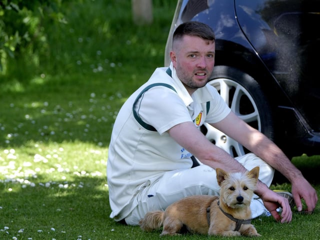 A cricketer watches the action alongside a canine companion