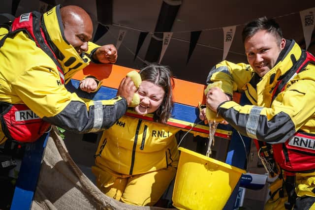 Crew members Ali Hussein and Niall Fagan soak Emily Clarkson in the Whitby RNLI Flag Weekend stocks.