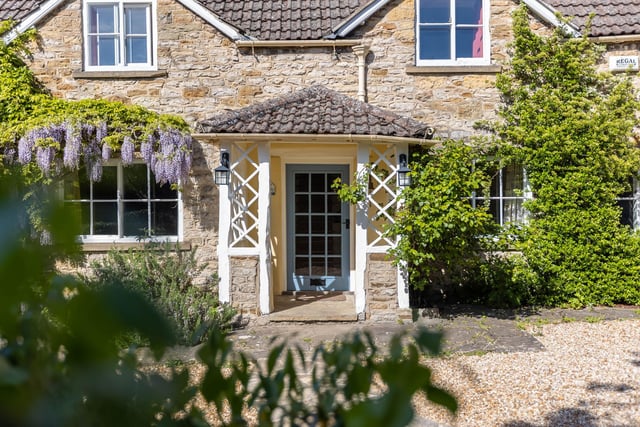 Welcoming wisteria blooms to one side of the cottage front door