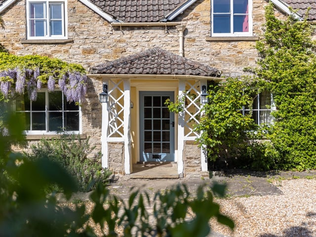 Welcoming wisteria blooms to one side of the cottage front door