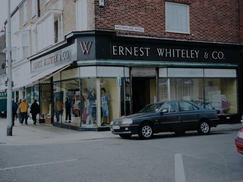 This is an old photo of the shops frontage during its heyday, depicting a gorgeous vintage car going by.