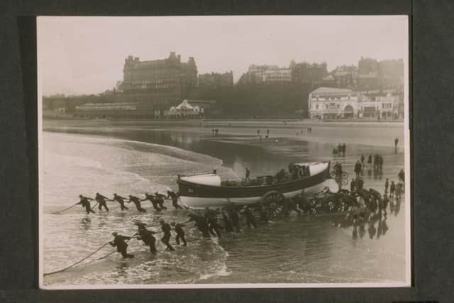 Scarborough. Self-Righting Motor Class. ON 683. Herbert Joy. Lifeboat on a trailer being launched on a sandy beach. People are pulling it into the water with four long ropes while others push from behind. July 1929 (Donor: Gift of Alexander O'Joy Hyde Park Gate London in memory of his brother Herbert who had drowned in Scarborough\'s South Bay). Credit: RNLI Archive