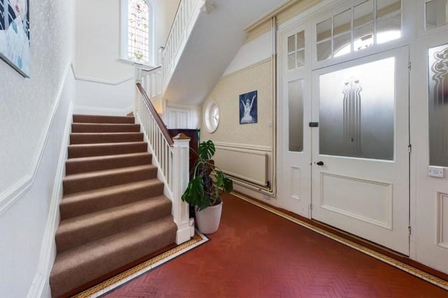 The entrance hallway with staircase leading up, and an original stained glass window at the turn of the stairs.