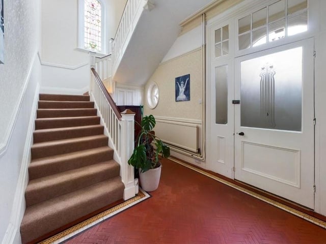 The entrance hallway with staircase leading up, and an original stained glass window at the turn of the stairs.