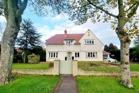 A front view of the detached home, within its lawned gardens.