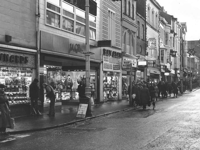 A sign for "Rudies Nightscene", beneath the clock, and a trio of menswear shops – John Collier, Ray Alan and Dunn & co. pictured in December 1983.