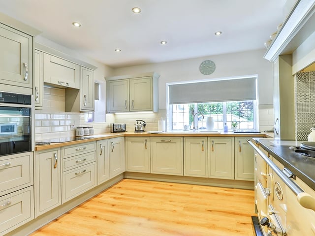 A contemporary style kitchen has fitted, pale green units and oak work tops. An Aga range cooker has a built-in electric oven and an electric hob with extractor, and there's an integral dishwasher.