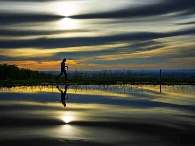A walker on his daily exercise passes a dew pond close to West Heslerton near Malton on the Yorkshire Wolds Way footpath.