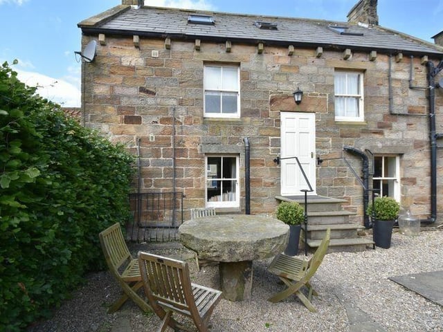 Steps lead down from the property to the rear garden with seating areas enclosed by tall hedging.