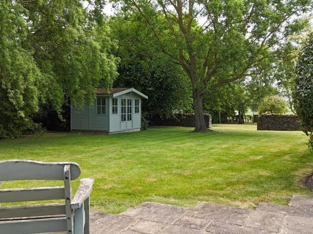 Lawned gardens fringed by trees have open fields beyond.