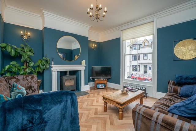 The living room, with log burner, has herringbone wood flooring.