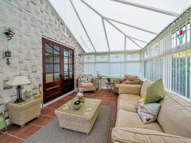 The conservatory has views of the garden, with doors leading outside.