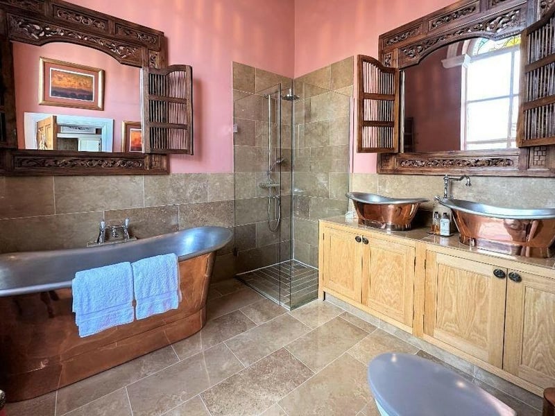 This en suite to the master bedroom has a roll top copper bath and double sinks crafted out of fossilized wood.