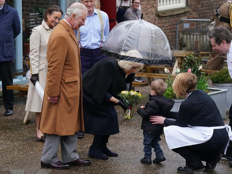 An adorable child hands the Queen Consort Camilla a lovely bunch of daffodils.