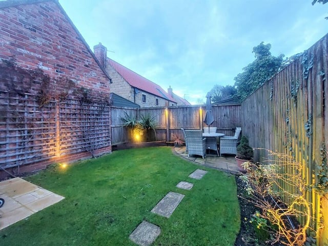 This lawned garden with feature lighting has patio seating areas.