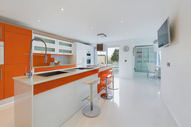 A sleek and shiny modern kitchen with large central island, on the upper ground floor.