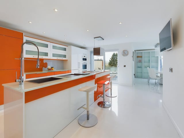A sleek and shiny modern kitchen with large central island, on the upper ground floor.