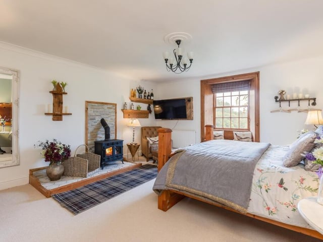 A double bedroom with window seat is made cosy by a log burner.