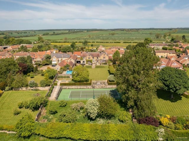 A view towards and over the property in its glorious setting, with the sunken all-weather tennis court in the foreground.