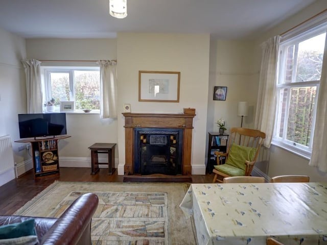 This sitting room, with stripped and varnished wooden floor, has a fireplace with oak surround, and a sash window.