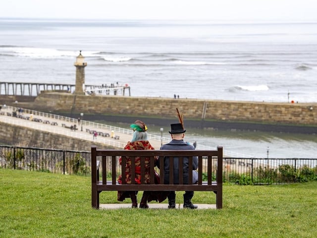 A couple dressed up for Whitby Steampunk Weekend are pictured sitting on a bench overlooking the beach.