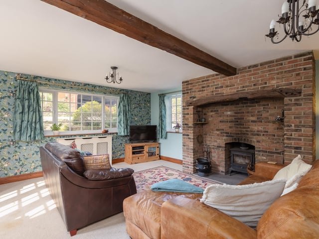 A rustic style beamed living room, with feature brick fireplace and cosy wood burning stove.