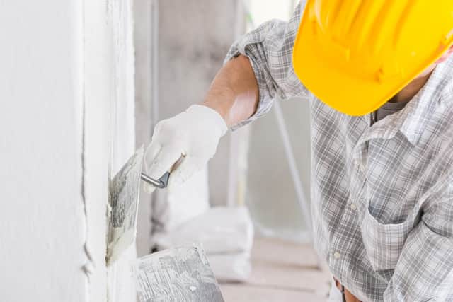 A builder uses a trowel to add plaster to a white wall during repairs for a damp area caused by water leakage or moisture