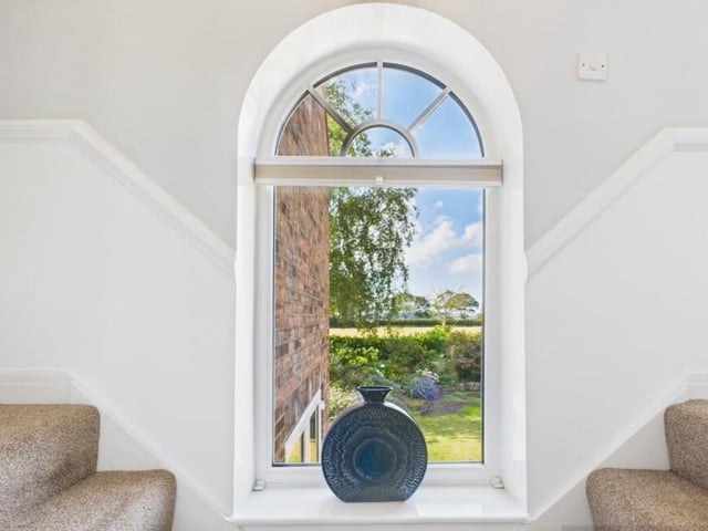 A feature arched window reveals gardens with fields beyond.