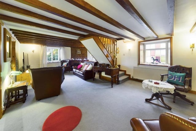 A spacious lounge has a beamed ceiling and open fire with stone surround. It features an original cooking range, and has built in display cupboards, and a stained glass window.