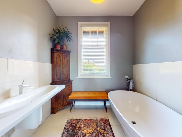 A free standing bath and matching wash basin form part of the suite within this well lit bathroom.
