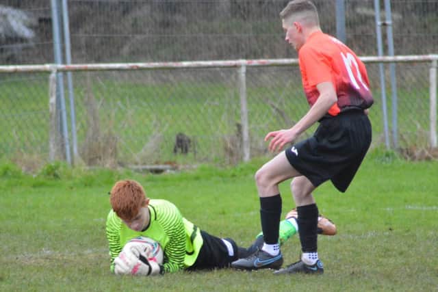 The Heslerton U16s keeper saves bravely at a Dragons forward's feet.