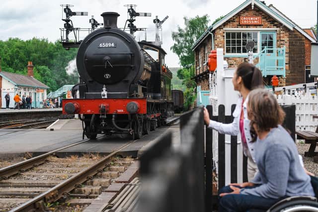 Man and woman at Grosmont Station, watching a heritage train pass.