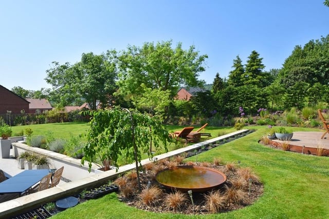 The established garden is bordered by trees and includes a water feature.
