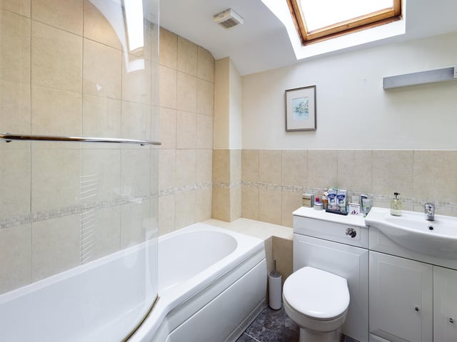 A wash basin within vanity unit, and bath with shower are included within this modern suite.