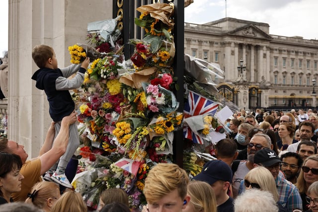 People pay their respect by placing flowers into the ironwork of a gate outside of Buckingham Palace following the death of Queen Elizabeth II. (Photo by Chip Somodevilla/Getty Images)