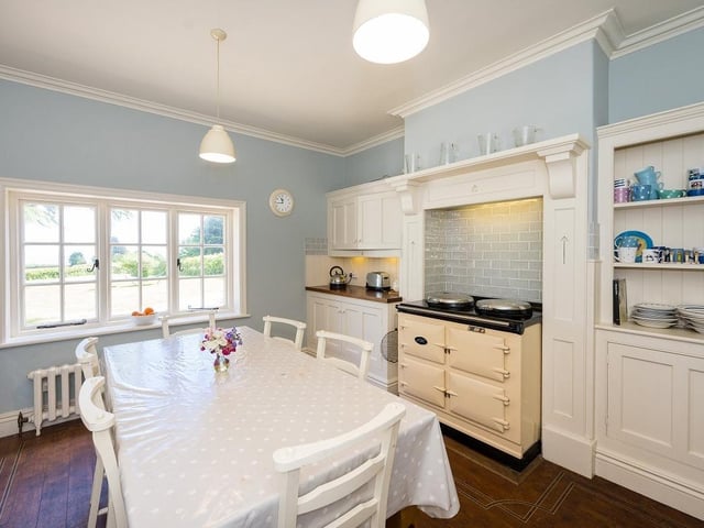 A dining kitchen with bespoke Shaker-style fitted cabinetry, Aga and views over the gardens and coastline.