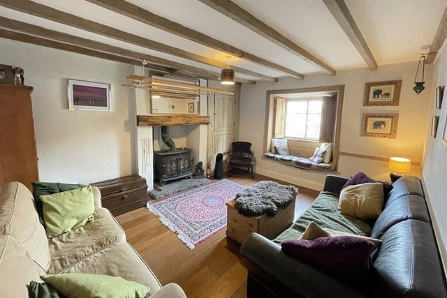 A cosy beamed sitting room with central fireplace and stove, and a charming window seat.