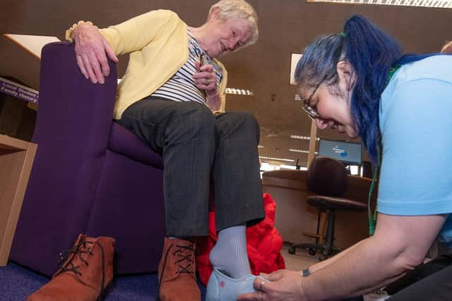 Library visitor Joan Tarren trying out slippers with outreach librarian Charlotte Simpson.