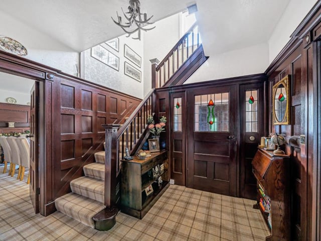 The hallway has wood panelled walls and stained glass detail to the windows.