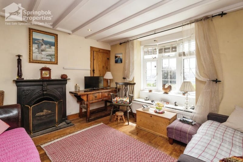 The beamed living room with wooden floor has a feature fireplace, and a bay window.