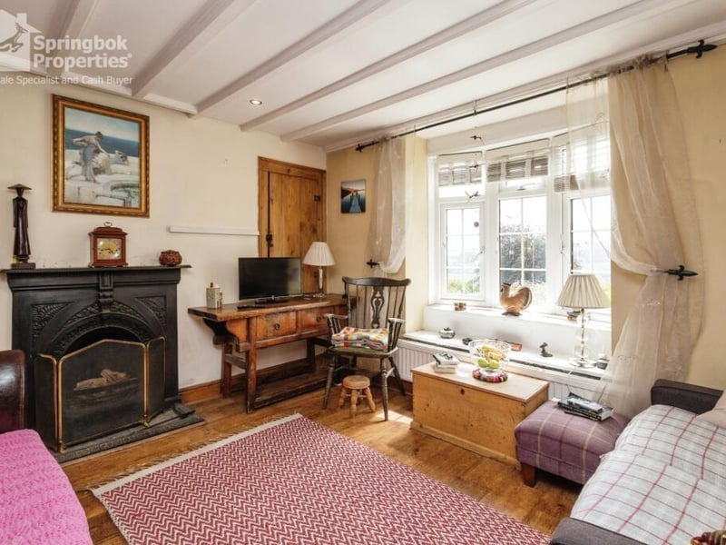 The beamed living room with wooden floor has a feature fireplace, and a bay window.